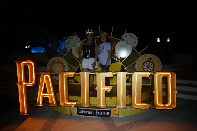 Photo Opp iluminado durante la noche, con dos personas en la plaza disfrutando del Carnaval de Mazatlán 2026.