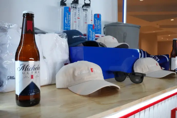 Merchandising Michelob Ultra: gorras y accesorios Gorras, lentes de sol, botella y bolsas con branding Michelob Ultra sobre mostrador de activación