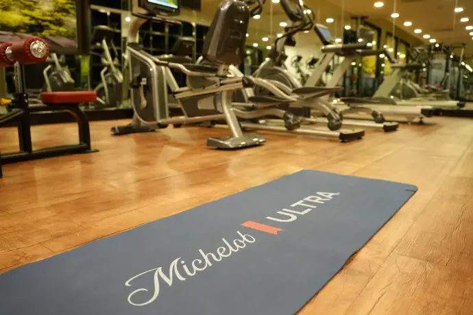 Tapete de yoga Michelob Ultra en gimnasio Tapete de yoga con logo Michelob Ultra sobre piso de madera en gimnasio de hotel, parte del takeover Mundial 2026