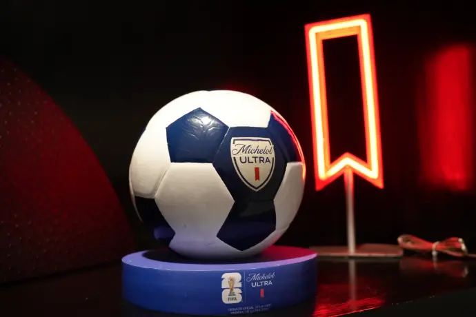 Balón Michelob Ultra con ribbon de neón Balón de fútbol con logo Michelob Ultra sobre base circular con isotipo FIFA World Cup 26, junto a ribbon de neón rojo